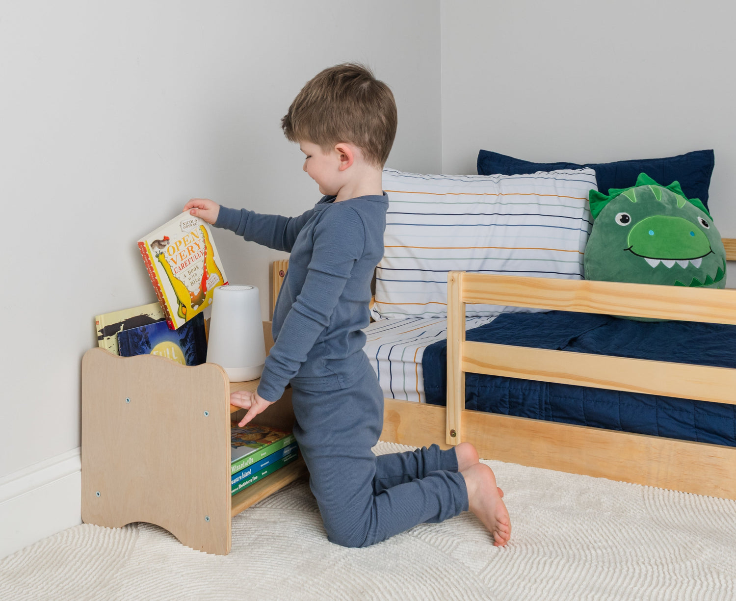 Toddler picking a book from his own Montessori nightstand with book pocket