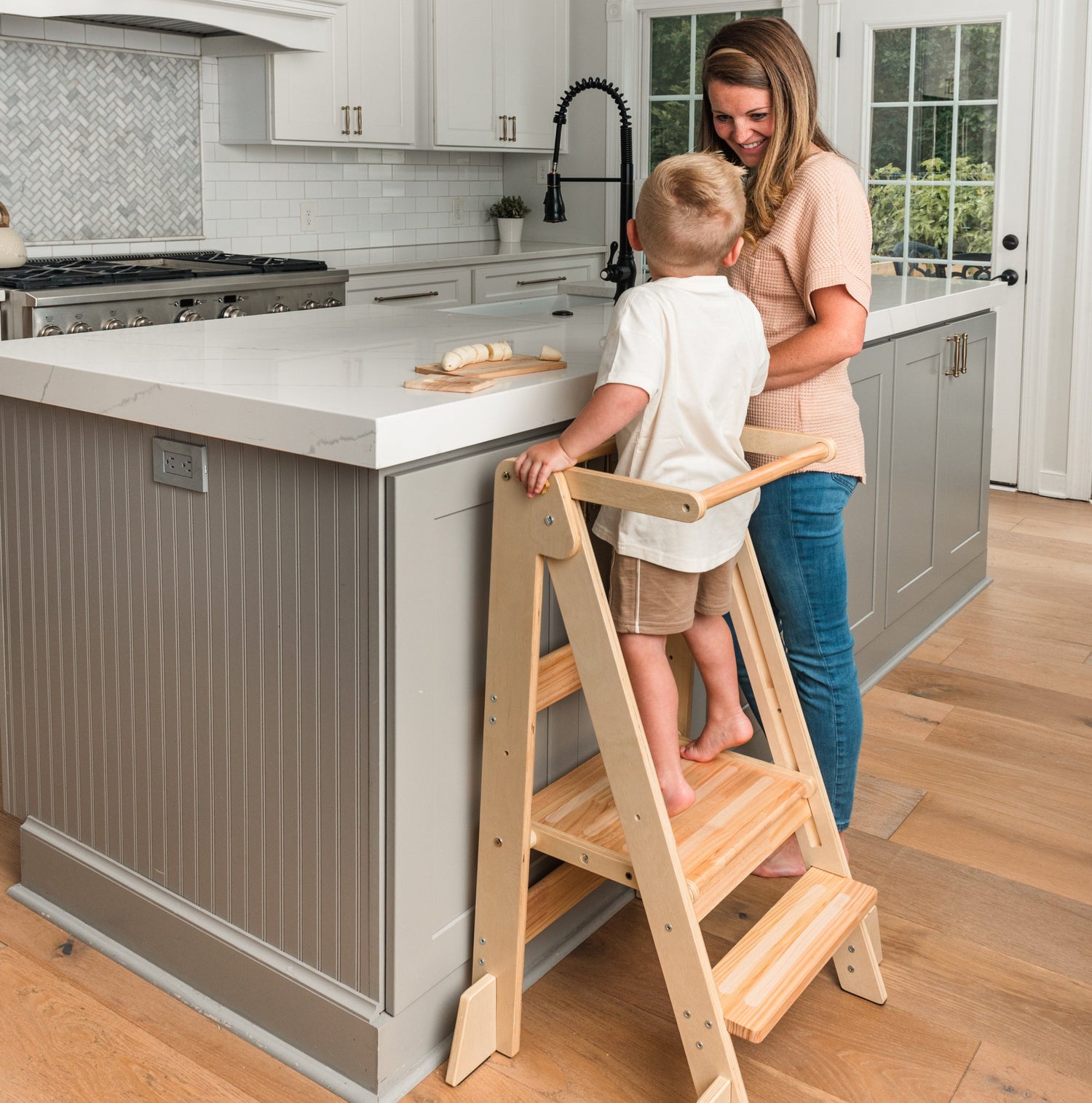Mother and child using a wooden foldable toddler tower in a kitchen