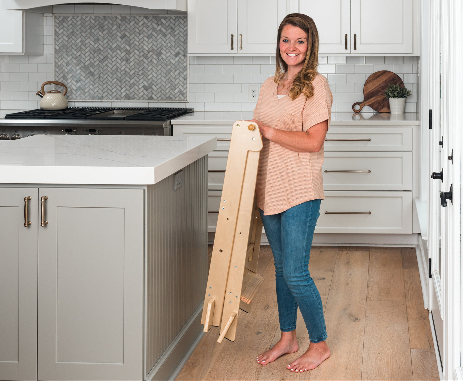 Woman holding a Ocodile foldable wooden toddler tower in a kitchen