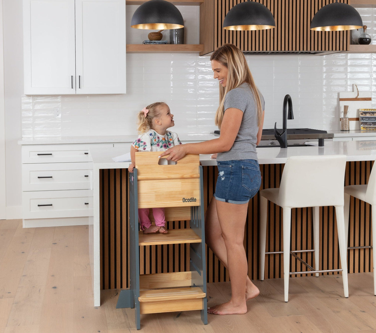 Mother and child using a wooden Ocodile toddler tower in a modern kitchen.